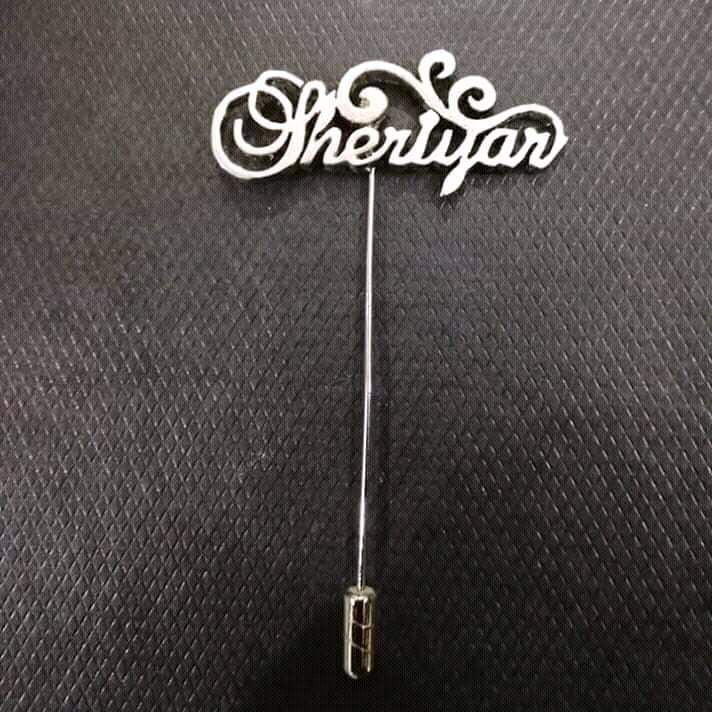 Silver brooch with 'Sherlyan' text on a textured black background
