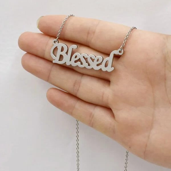 Silver 'Blessed' necklace held in a hand against a white background
