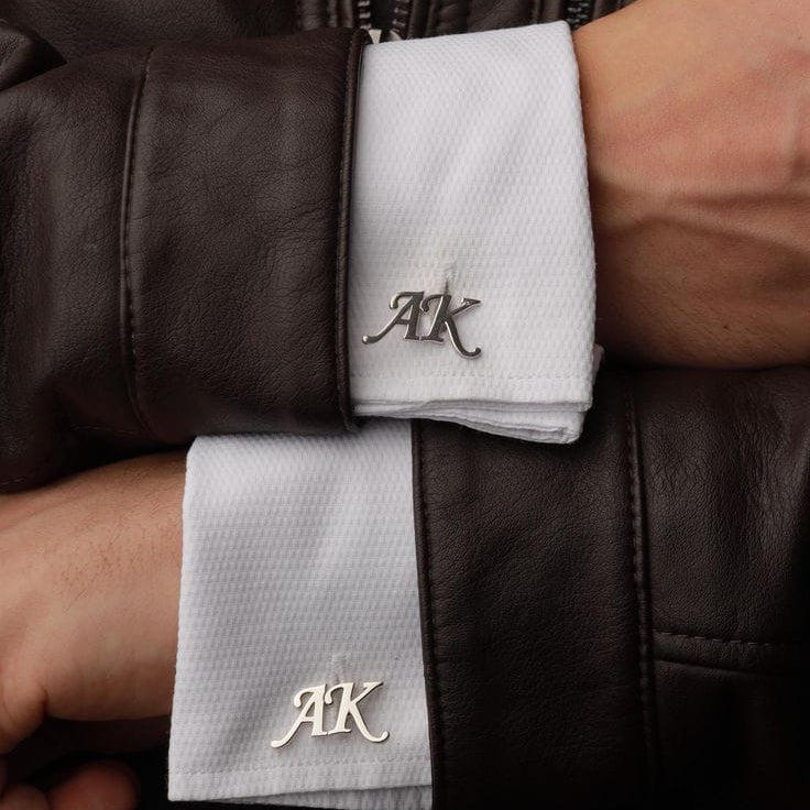 Close-up of a person wearing white cufflinks with 'AK' initials on a dark jacket.