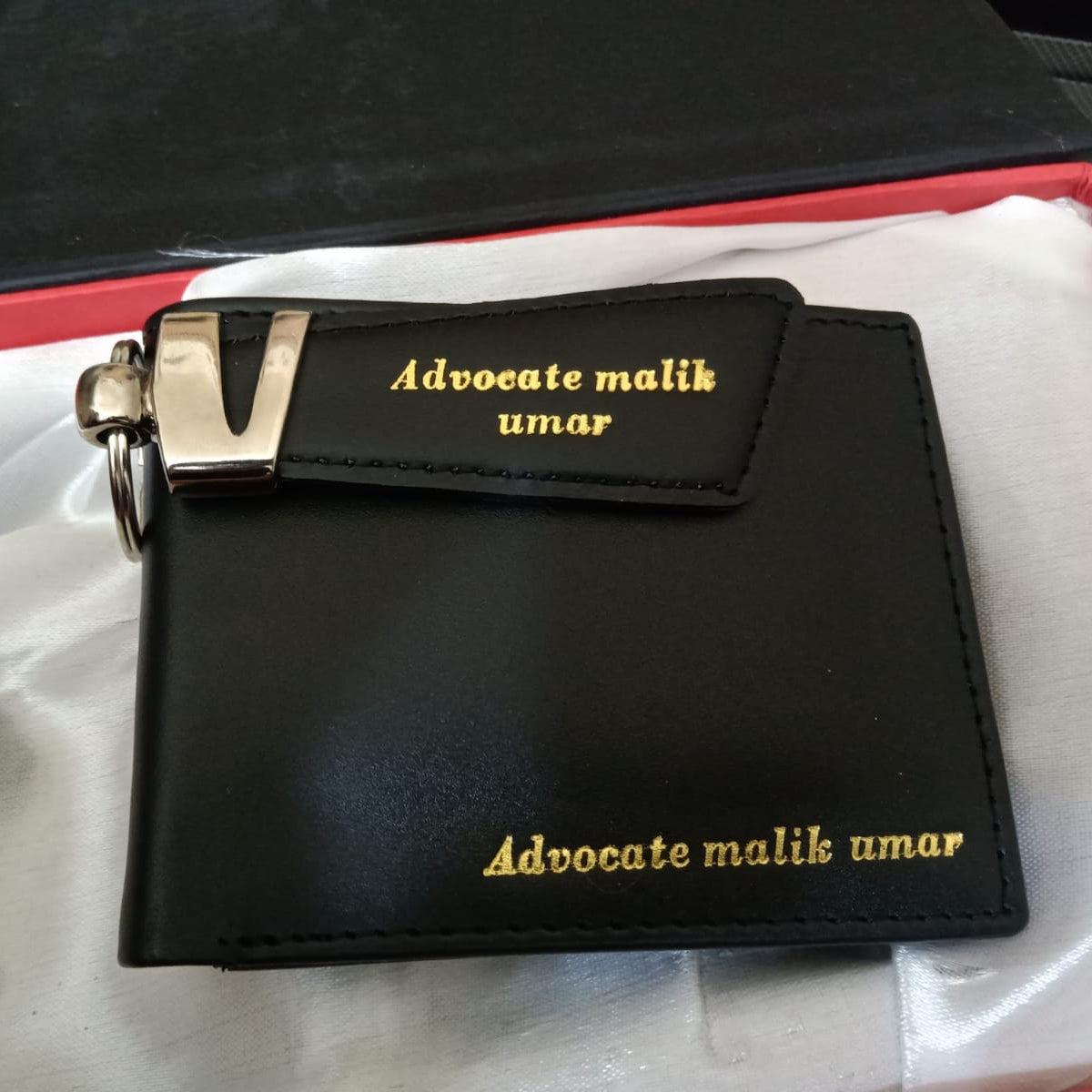 Black wallet with gold text 'Advocate malik umar' on a white surface
