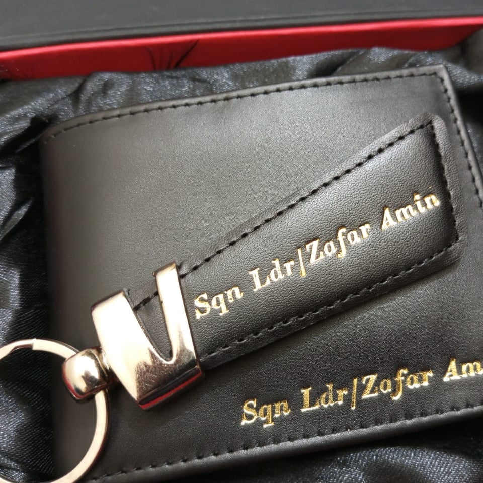 Black leather wallet with keychain and engraved text on a black satin background