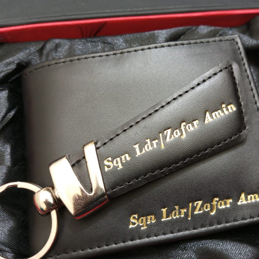 Black leather wallet with keychain and engraved text on a black satin background